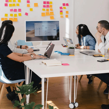 A group of people sitting around an office table looking at a monitor